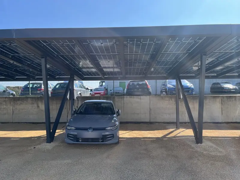 Voiture électrique garée sous une ombrière photovoltaïque réalisée par JCBO Toit ENR